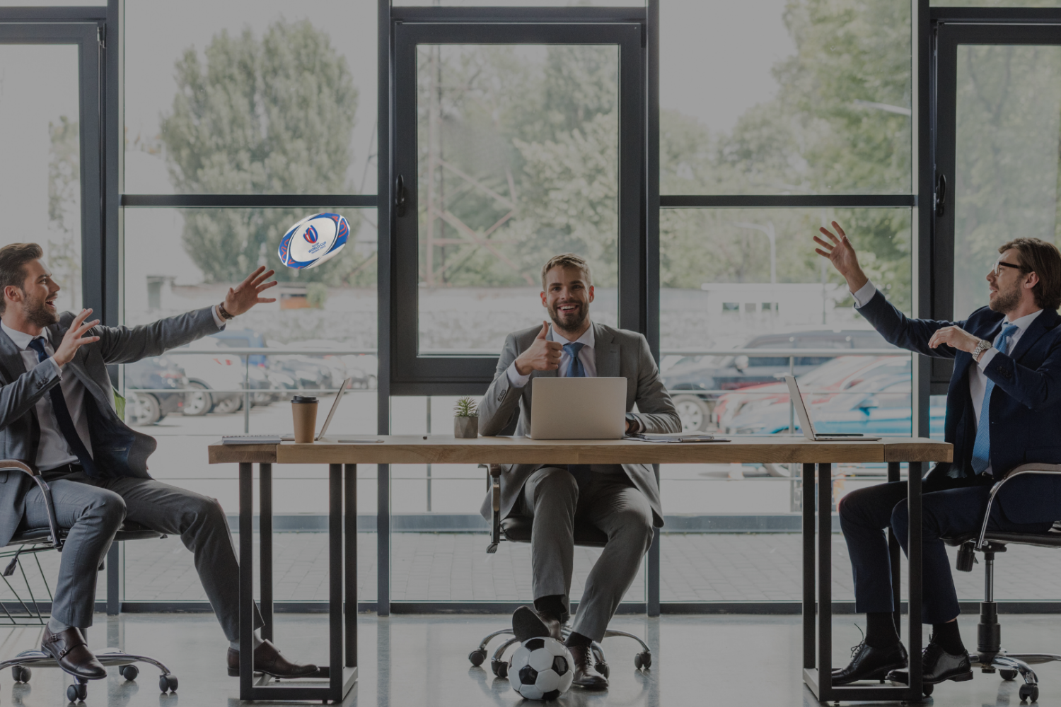 Three men at their desks in an office throwing a rugby ball in the air