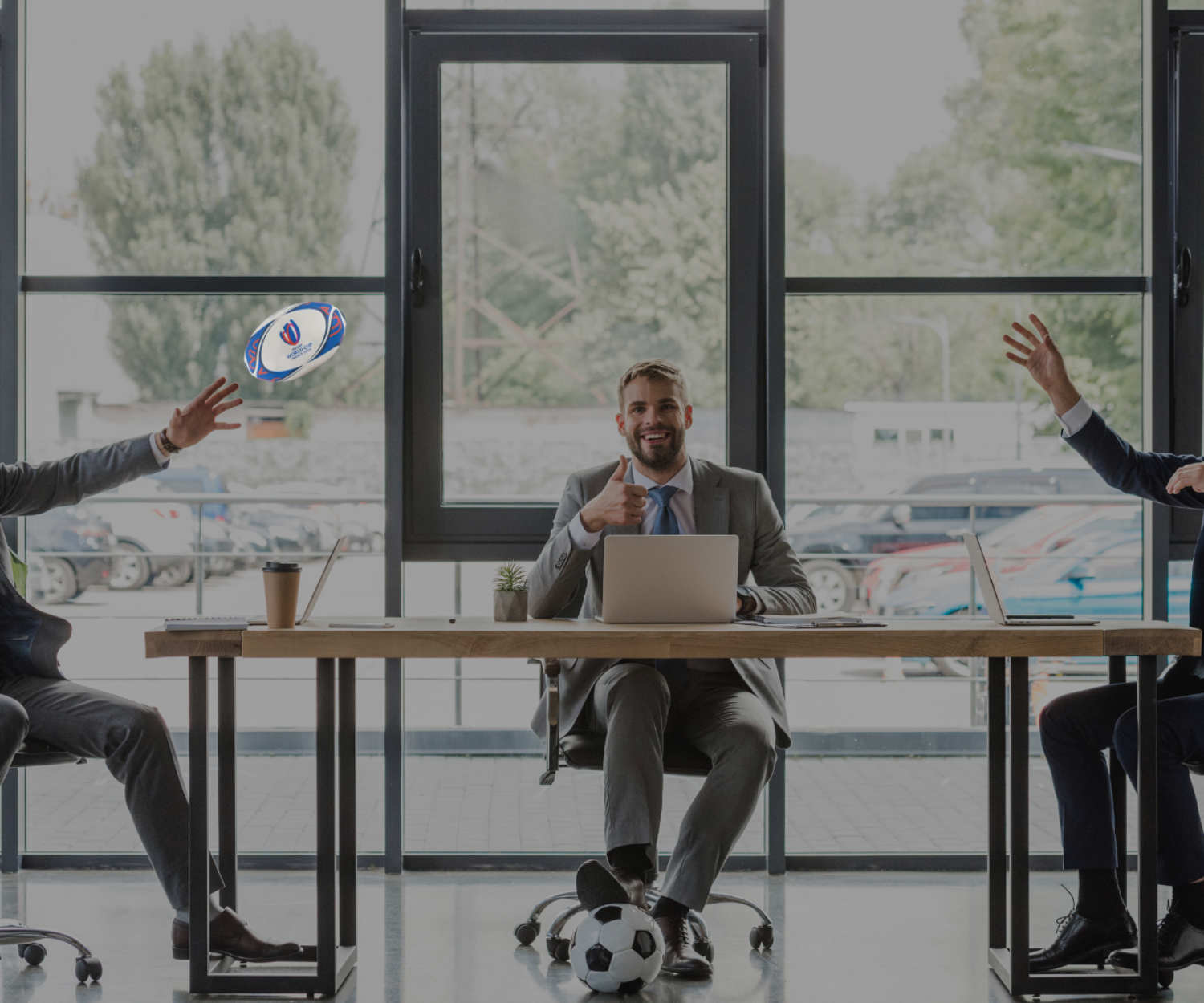 Three men at their desks in an office throwing a rugby ball in the air