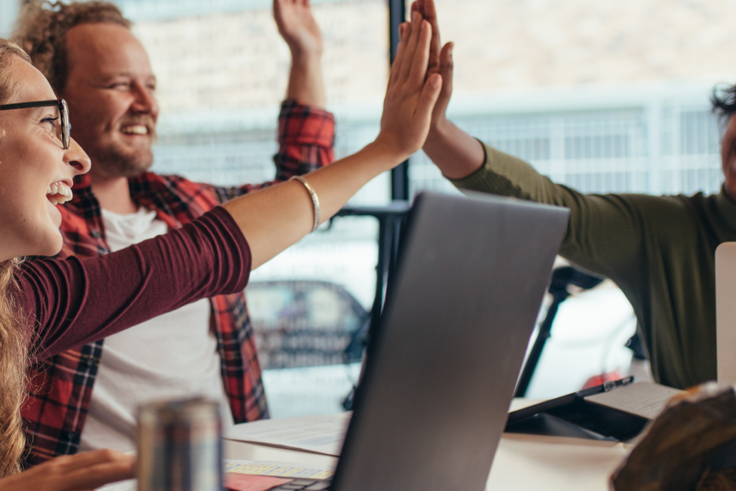 3 colleagues high fiving at their desks.