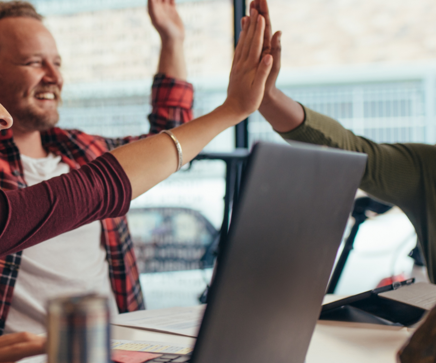 3 colleagues high fiving at their desks.