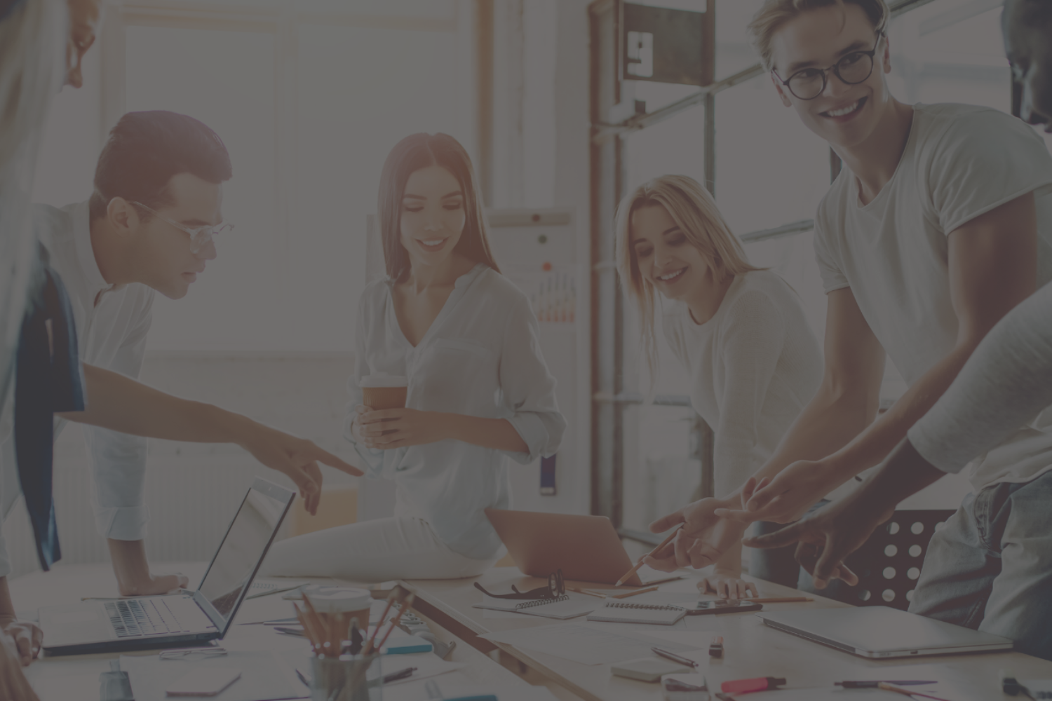 Stock image of young people in an office, standing at a table discussing a project.