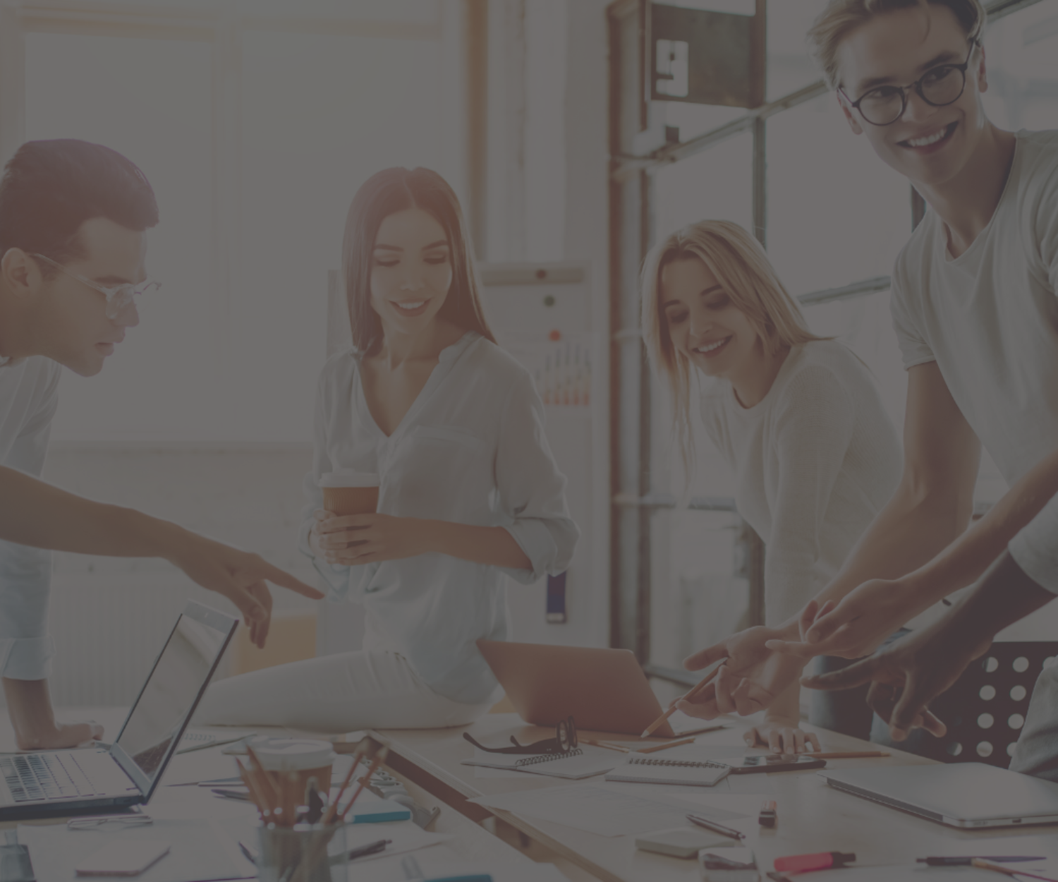 Stock image of young people in an office, standing at a table discussing a project.