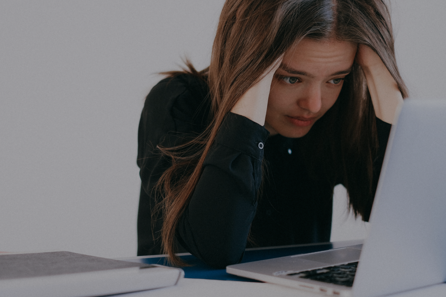 Stock image of a person looking at a laptop with their head in their hands, overwhelmed at the amount of emails they have.