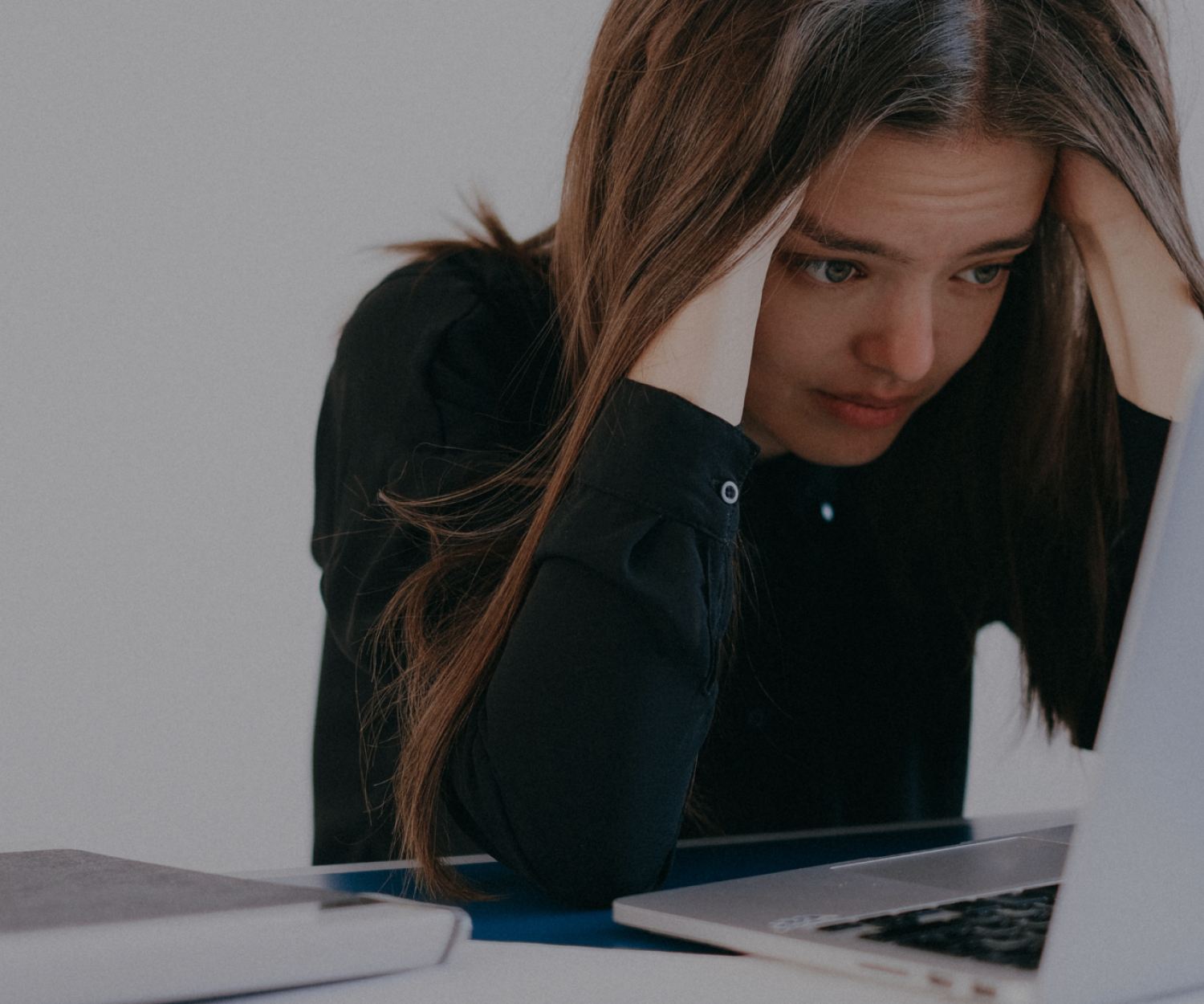 Stock image of a person looking at a laptop with their head in their hands, overwhelmed at the amount of emails they have.